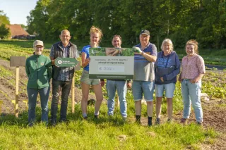Zeven mensen van De Kleine Boerderij op een rij met een cheque in handen